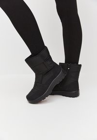 Botas de invierno aislantes negras con un upper texturizado, cierre de cremallera y una suela gruesa con un patrón de relieve para el agarre.
