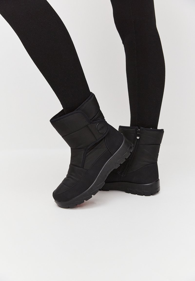 Botas de invierno aislantes negras con un upper texturizado, cierre de cremallera y una suela gruesa con un patrón de relieve para el agarre.