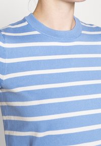 Randig kortärmad topp i ljusblått och vitt, tillverkad av mjukt tyg. Har en ribbad rund halsringning och ett horisontellt randmönster.