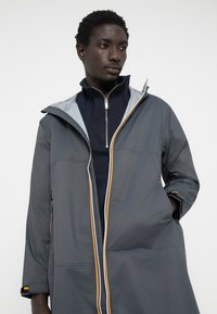 Hall Gray veekindel jakk kapuutsiga, kontrastse tõmbluku ja värvilise detailiga. Omab lõdva istuvust ja sujuvat tekstuuri.