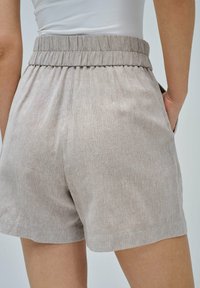 Pantalones cortos de punto acanalado beige con cintura elástica y bolsillos laterales, combinados con una blusa blanca ajustada que muestra la parte media del muslo y la cintura.
