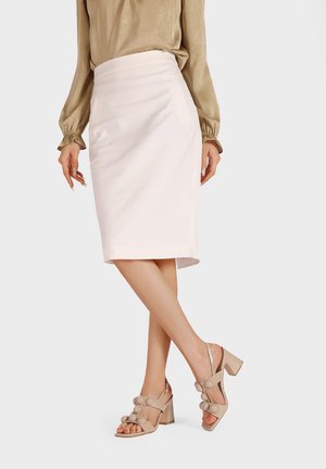 Donna che indossa una camicetta beige, una gonna a tubino bianca al ginocchio e sandali beige con tacco alto e decorazioni rotonde.