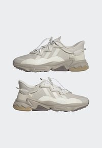 Des chaussures de course avec une tige en tissu gris clair, une semelle intermédiaire texturée, des lacets réfléchissants et une semelle extérieure en caoutchouc avec un design ondulé pour une meilleure adhérence.