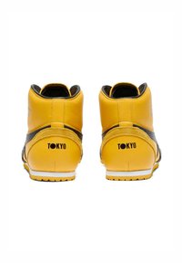 Žluté vysoké tenisky mají strukturovaný kožený svršek, černé detaily a bílou gumovou podrážku. Na patách je vytištěno "TOKYO".