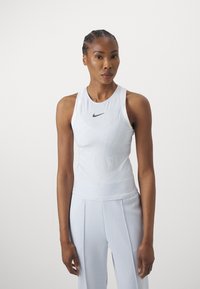 Fehér sportos atlétikai trikó struktúrált mintázattal és fekete Nike pipa logóval. Fényes szürke sportnadrággal kiegészítve.