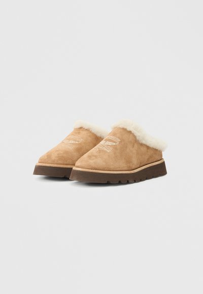 Sapatos slip-on de camurça castanha com um colarinho fofinho branco e sola de borracha texturizada. Apresenta um detalhe de costura simples na parte superior.