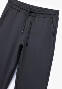 Sorte sweatpants med en glat tekstur, elastisk talje, justerbar snor og sidelommer. Letvægtsstof.