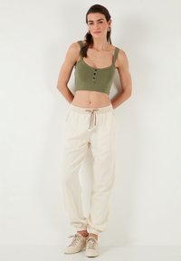 Olijfgroen geribbelde crop top met knoopdetails, gecombineerd met crèmekleurige tapered broek met een elastische tailleband en zijzakken.
