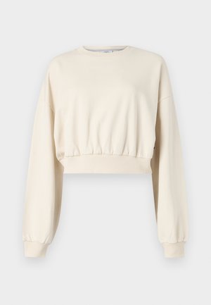 Afskåret, beige sweatshirts med lange, puffy ærmer. Har elastisk talje og ribbede manchetter. Diskret logo broderet nær halsudskæringen.