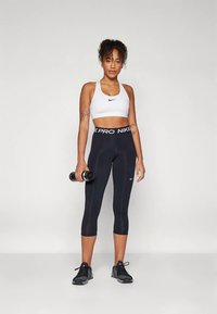 Zwarte Nike Pro legging met een wit Nike cropped top. De legging heeft een brede tailleband en een glad, rekbaar materiaal.