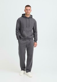 Grå fleece hætte trøje med snoretræk og kængurulomme, parret med matchende grå sweatpants, båret med hvide sneakers.