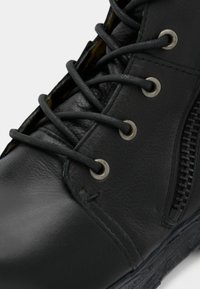 Black leather ankle boot featuring round laces, metal eyelets, and a side zipper for easy access. Textured surface detailing is visible.