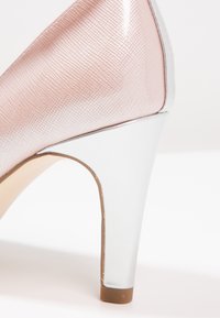 Scarpa con tacco alto di colore rosa, con un accento argentato lucido sul tacco. La parte superiore presenta un delicato motivo a griglia. Suola beige uniforme.