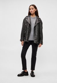 Melna ādas motociklista jaka ar sudraba aksesuāriem, uzvilkta virs pelēka džempera, kopā ar melnām džinsu biksēm un spīdīgām melnām kurpēm.