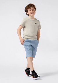 Beige short-sleeve t-shirt with logo, paired with light blue shorts and black sneakers featuring orange accents. Smooth fabric, relaxed fit.