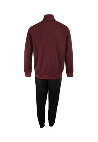 Tuta bordeaux composta da una giacca con zip e collo alto, maniche lunghe, abbinata a pantaloni neri, larghi, realizzati in tessuto morbido.