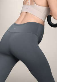 Visoke sivo legice z gladkim, raztegljivim materialom. Minimalistična zasnova vključuje subtilen logotip na pasu in brezšivno konstrukcijo.