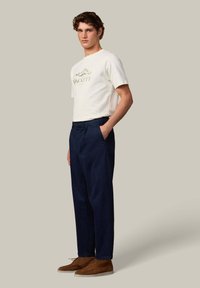 Witte korte mouw t-shirt met bergafbeelding en tekst, gecombineerd met marineblauwe broek en bruine suède schoenen. Eenvoudig, op maat gemaakt ontwerp.