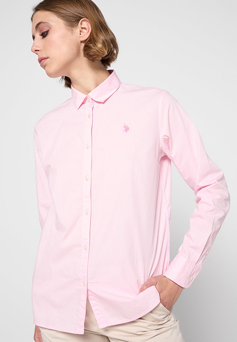 Chemise boutonnée rose clair à manches longues, col, texture subtile, logo brodé sur la poitrine gauche et ourlet droit.