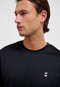 Zwarte T-shirt met korte mouwen van gladde stof, een ronde halslijn en een wit chevronlogo aan de linkerkant van de borst.