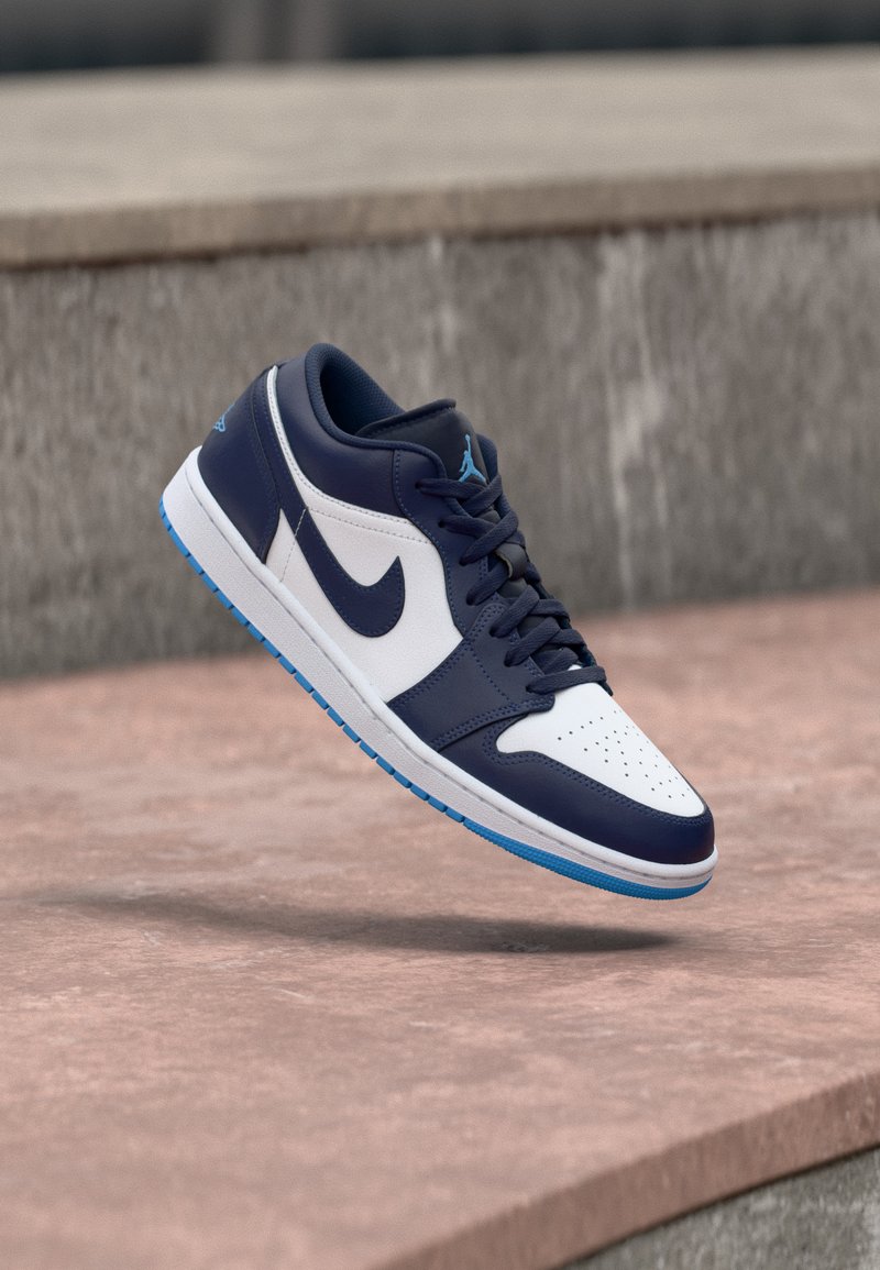 Baskets Nike Air Jordan bleu marine et blanches flottant au-dessus de marches en béton, montrant le profil latéral et des accents bleus sur la semelle.