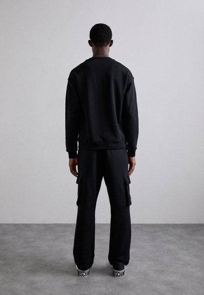 Čierna mikina a cargo nohavice vyrobené z mäkkej látky. Medzi funkcie patrí rebrované manžety, bočné vrecká a detaily loga na obuvi.