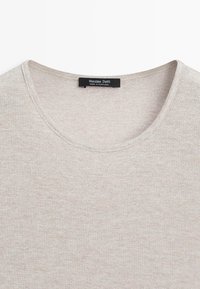 Beige gebreide trui met een ronde hals en een zwart label met de tekst "Massimo Dutti, Made in Portugal" dat aan de binnenkant van de kraag is genaaid.