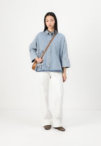 Ljusblå denim oversize-skjorta med framknappling, sidofjädere detaljer, vita vida byxor och skor med leopardmönster, kompletterat med en brun axelväska.