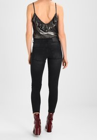 Jeans skinny negros combinados con una camiseta de tirantes plateada metálica que cuenta con un escote con volantes. La modelo lleva botas de tacón altas en burdeos.