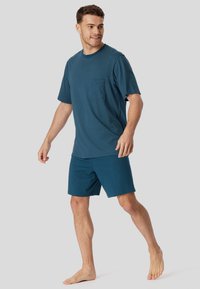 Männer Sportbekleidung mit einem türkisfarbenen Kurzarmshirt mit Punktmuster und passenden türkisfarbenen Shorts, aus leichtem Stoff gefertigt.