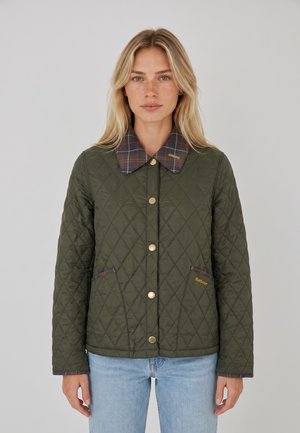 Femme portant une veste matelassée vert olive avec un col à carreaux, des boutons dorés et des poches avant, associée à un jean bleu clair.