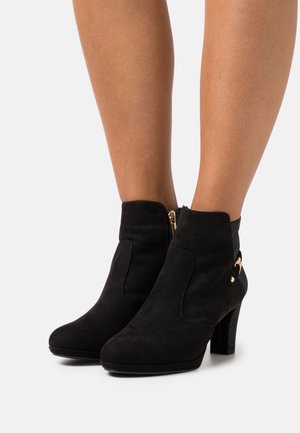 Schwarze Wildleder-Stiefel mit Knöchelhöhe, strukturiertem Absatz, Reißverschluss und goldfarbenen Hardware-Akzenten. Runde Zehenpartie und taillierte Passform am Knöchel.