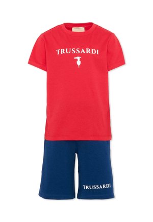 T-shirt rossa a maniche corte con la scritta "TRUSSARDI" e logo bianco, abbinata a pantaloncini blu navy con scritta "TRUSSARDI" sulla gamba sinistra.