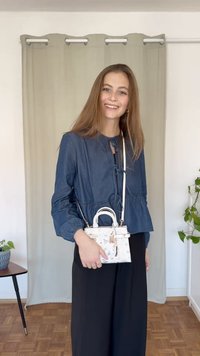 Denim bluzka z nabranim pasom in vezanjem okoli vratu, v kompletu z belo mini torbico, ki ima teksturiran vzorec in zlate dodatke.