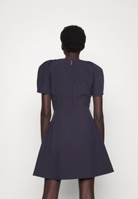 Kniekurzes, marineblaues Kleid mit Puffärmeln, tailliertem Oberteil und schwingendem Rock. Mit einem Reißverschluss hinten und glattem, strukturiertem Stoff.