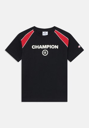 Μαύρο κοντομάνικο μπλουζάκι Champion με κόκκινες διακριτές επενδύσεις στους ώμους, λευκό λογότυπο στο κέντρο του στήθους και μικρό λογότυπο στο αριστερό μανίκι.