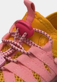 Baskets jaunes avec lacets élastiques roses maintenus par un verrou rose et larges sangles roses sur un matériau en mesh respirant.