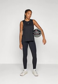 Czarny bezrękawnik z logo, zestawiony z czarnymi legginsami. Modelka trzyma piłkę do koszykówki z logo Jordana i nosi białe trampki.