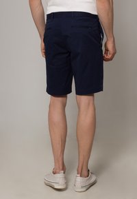 Tummansiniset puuvillahousut, suora malli ja sivutaskut. Yksinkertainen kangas ja reunapitoiset lahkeet. Yhdistetty vaaleisiin kenkiin.