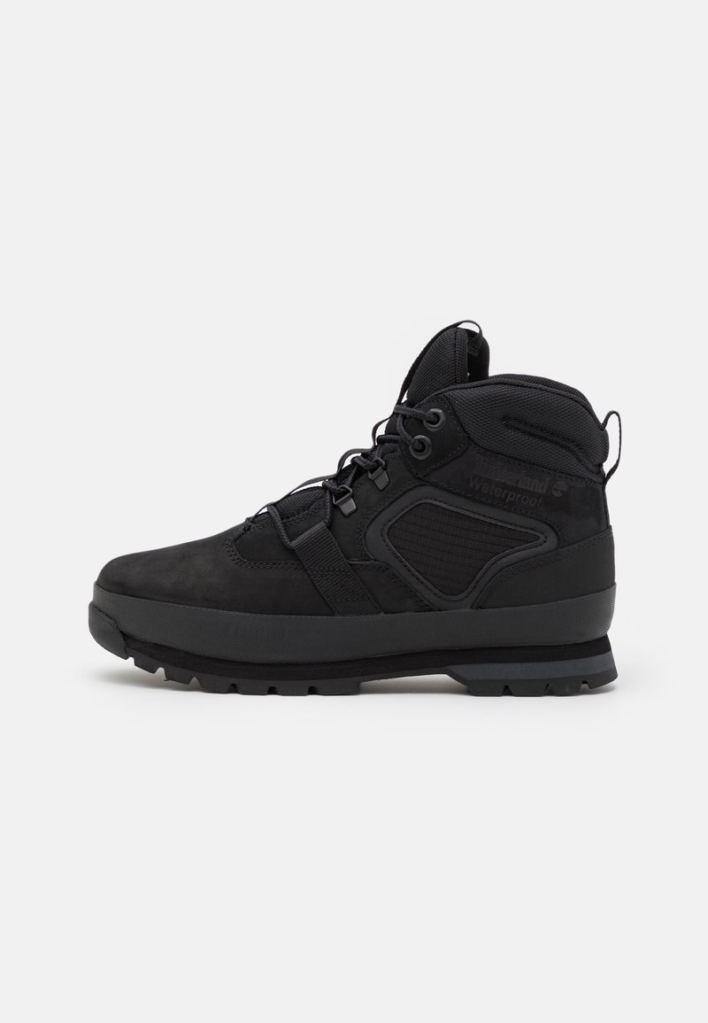 Botte de randonnée noire imperméable avec col rembourré à la cheville, lacets, semelle épaisse à crampons et languettes de traction au talon et à la languette, vue de profil latéral.