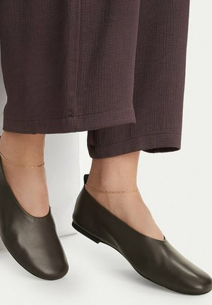 Dark brown cropped pants paired with olive green slip-on flats and thin gold anklets on both ankles.