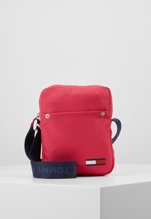 Sac bandoulière rectangulaire rouge avec poche avant et sangle réglable bleu marine sur fond blanc.
