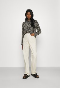 Top de manga longa em estampado de leopardo preto e branco, combinado com calças largas de cintura alta na cor crème e sandálias pretas de deslizar.