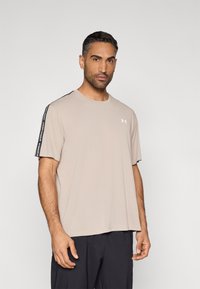 Beige sportstopp laget av lett stoff med svarte side-striper. Rund hals, korte ermer og en løs passform.
