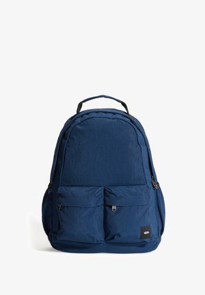 Sac à dos bleu foncé avec deux poches zippées à l'avant, une poignée supérieure et un patch logo Vans dans le coin inférieur droit de la poche avant.