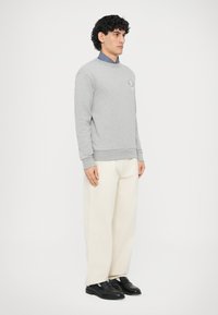 Szara bluza bawełniana z okrągłym dekoltem i ściągaczami przy rękawach, zestawiona z białymi spodniami o szerokich nogawkach i czarnymi butami.