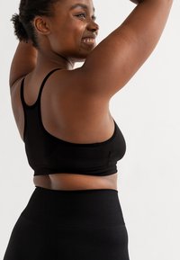 Schwarzer Sport-BH mit schlichtem Design und dünnen Trägern, kombiniert mit hochtaillierten schwarzen Leggings, die einen ribbeligen Bund haben.
