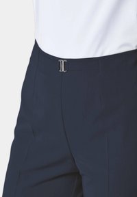 Pantalons bleu marine avec une coupe plate et une fermeture à verrou en métal, fabriqués dans un tissu lisse avec une coupe ajustée et des lignes épurées.