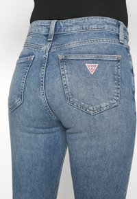 Vaaleansiniset farkut, joissa on muotoileva malli. Niissä on kaksi takataskua ja oikeassa taskussa kolmio punavalkoinen logo-patch.