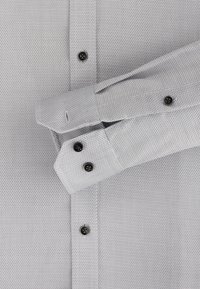 Lichtgrijze shirt met patroon en een gestructureerde stof. Bevat zwarte knopen en gestructureerde manchetten. Gestructureerd ruitpatroon over het gehele oppervlak.